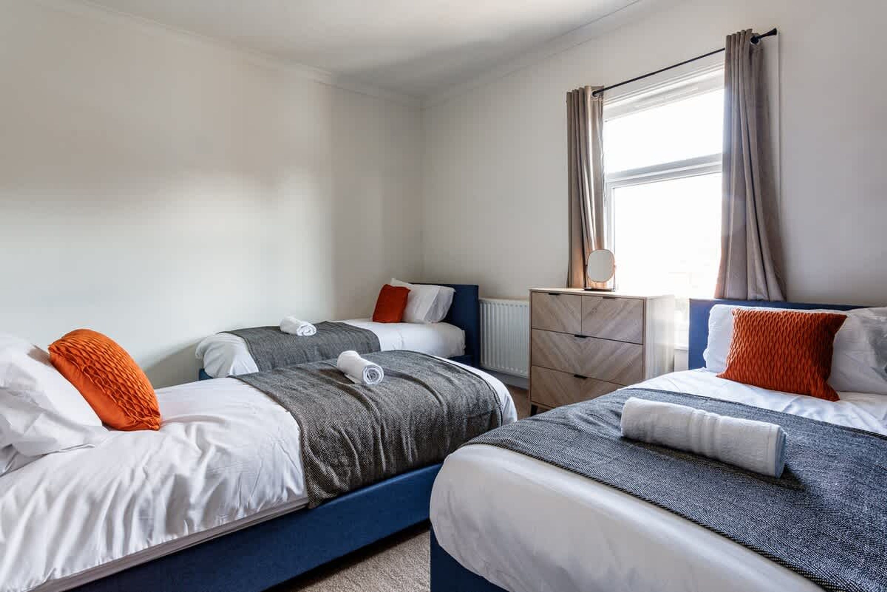 Een hotelkamer met twee bedden, een dressoir en een raam met gordijnen.