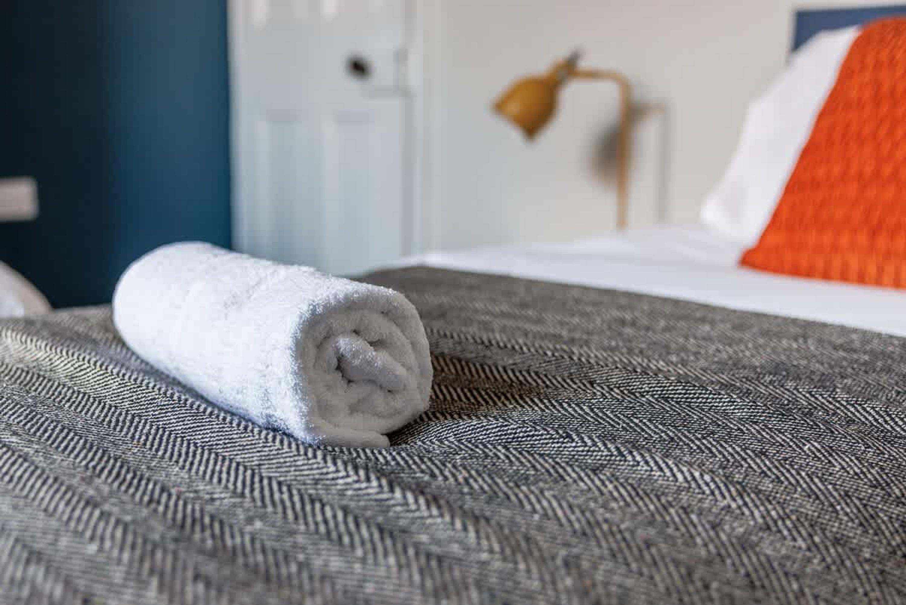 A neatly rolled white towel on a textured gray bedspread in a hotel room.