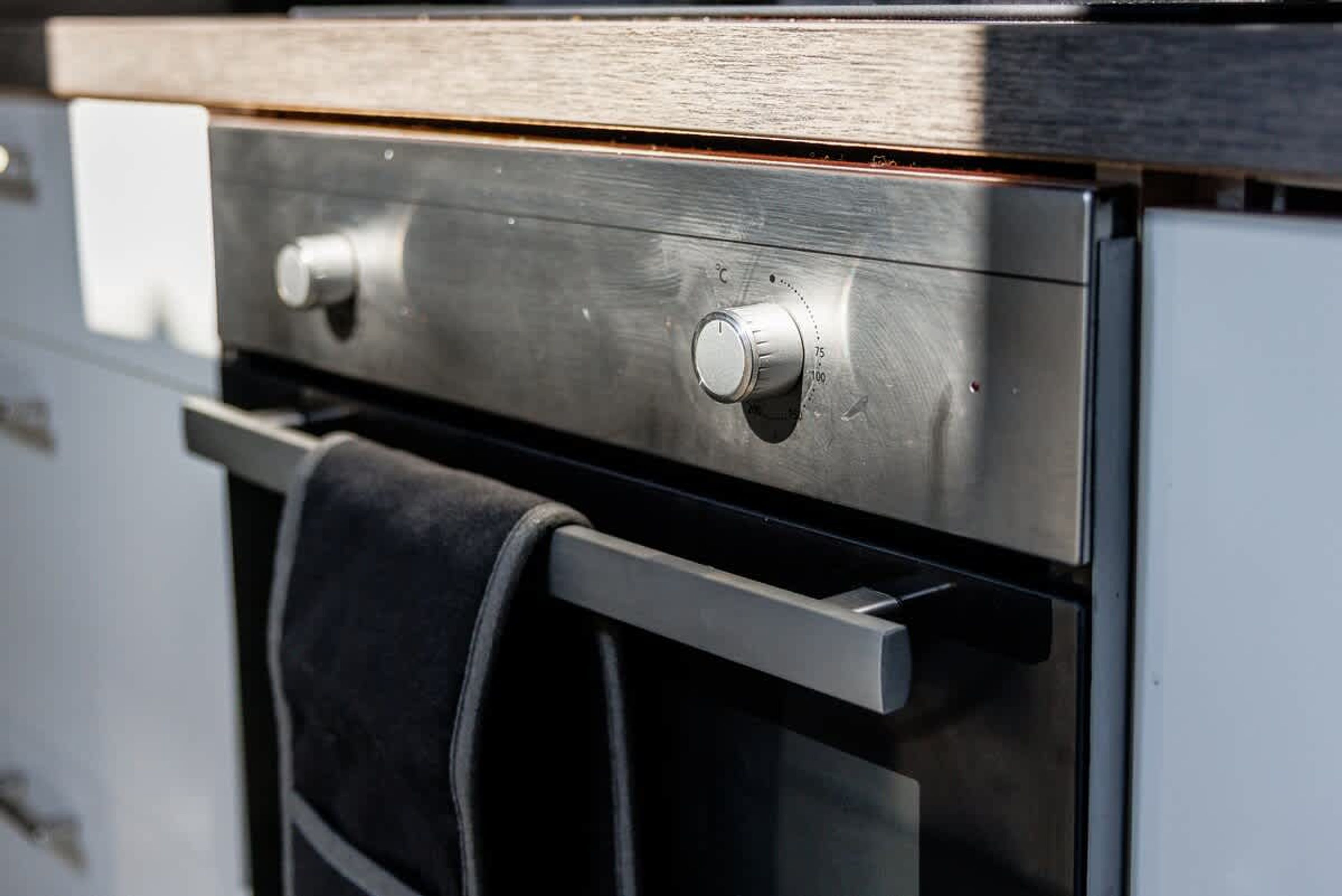 A stainless steel oven with a control knob and a towel hanging on the handle.