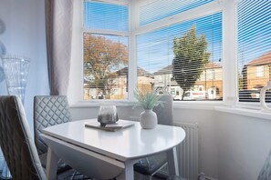 Ein Essbereich mit Tisch und Stühlen, einem Blumentopf und Blick ins Freie durch große Fenster.