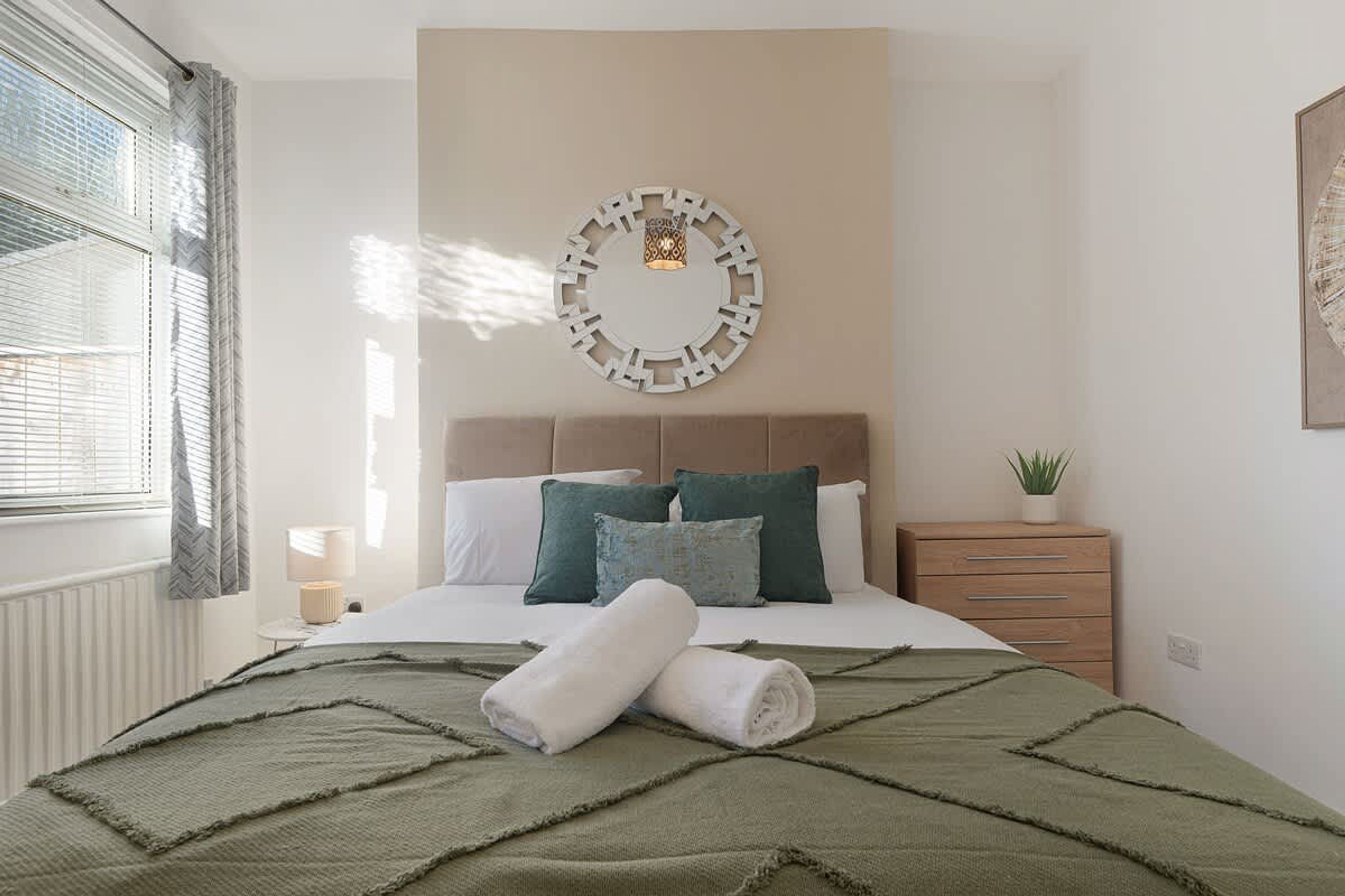 A bedroom with a bed, pillows, a bedside table, a lamp, and a wall decoration.