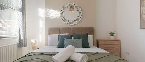 Un dormitorio con cama, almohadas, una mesita de noche, una lámpara y un adorno en la pared.