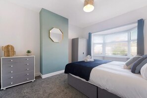 A bedroom with a bed, a dresser, a mirror, and a window with curtains. - Darlington Central 4BR With Parking and Free Wifi (Darlington)