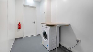 Een wasruimte met een wasmachine, een brandblusser en een deur.