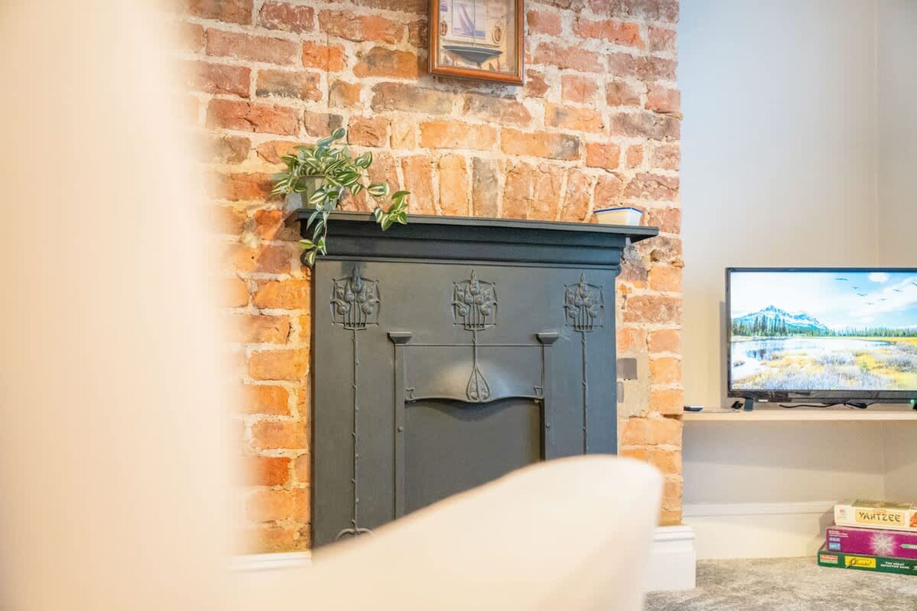 A brick fireplace with a mantel, a television on a stand to the right, and a plant on top.