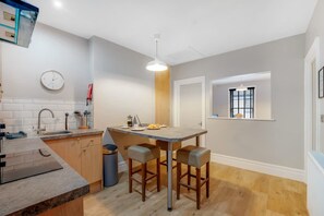 A modern kitchen with a central island, bar stools, a sink, and a window with blinds. - Spacious 1 Bedroom in Hartlepool With Wifi (Hartlepool)