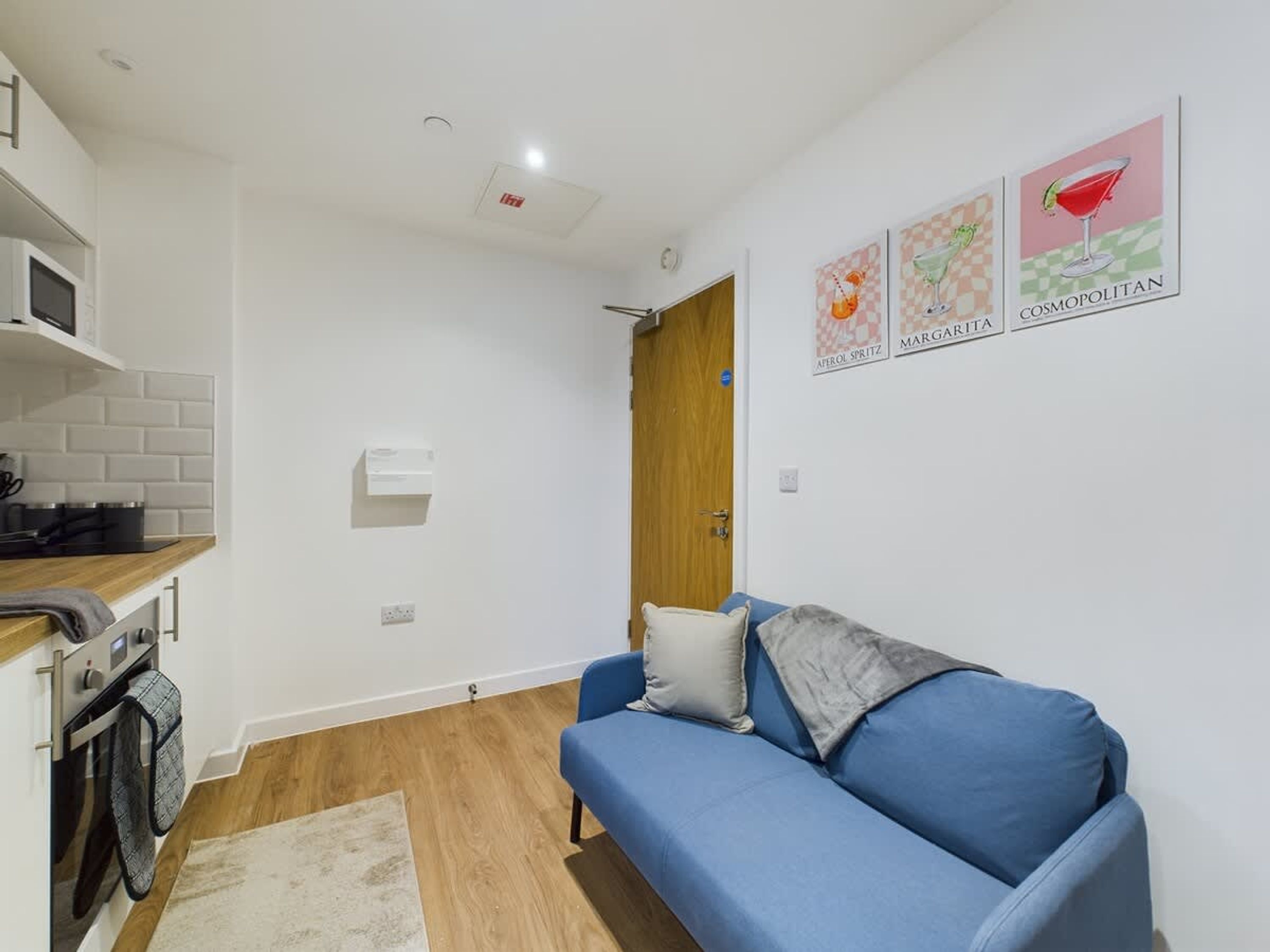 A compact living space with a kitchenette, a blue sofa, and a door leading to another room.