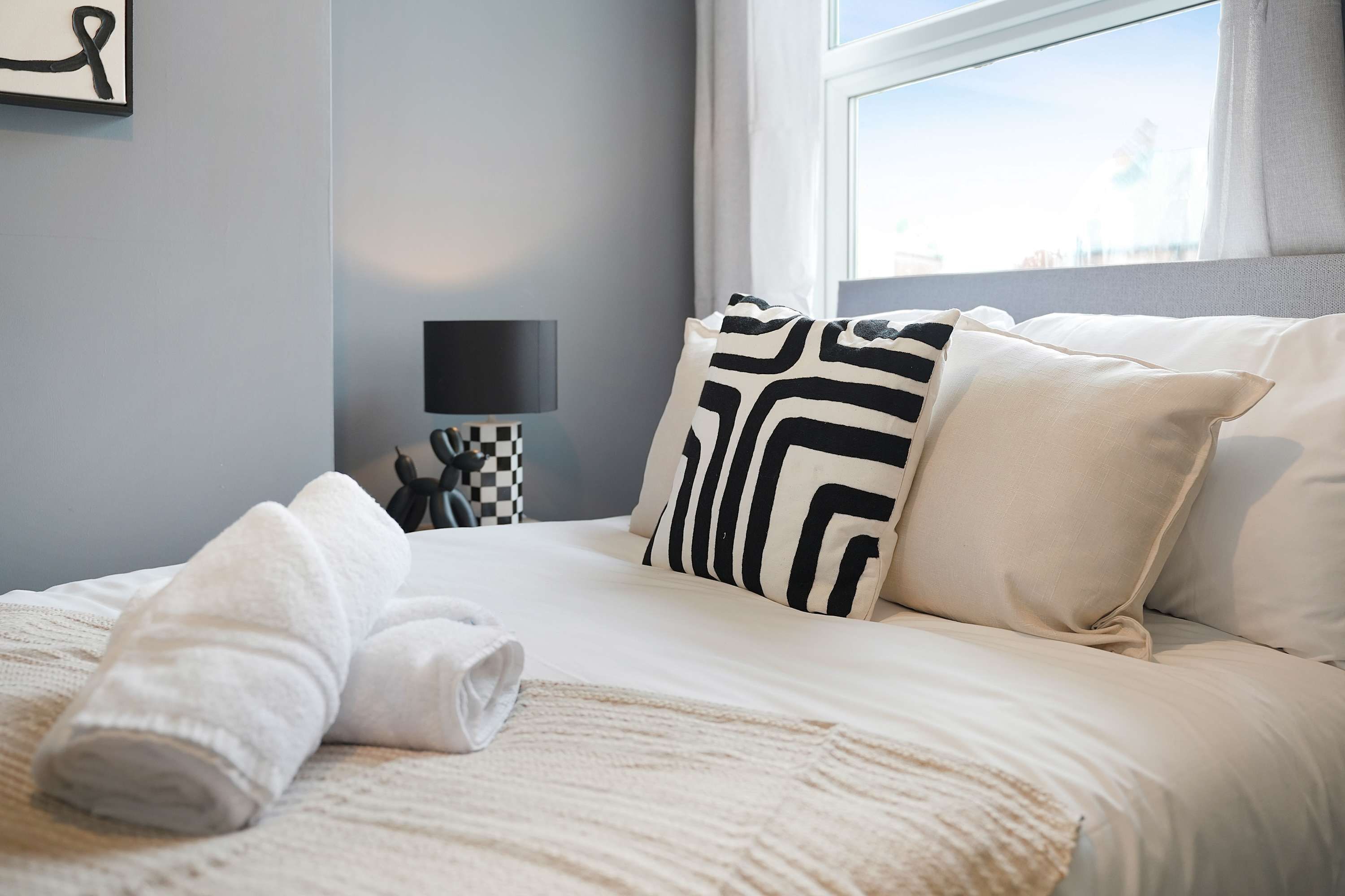 A neatly made bed with a checkered pillow, a bedside lamp, and a towel on the bed.