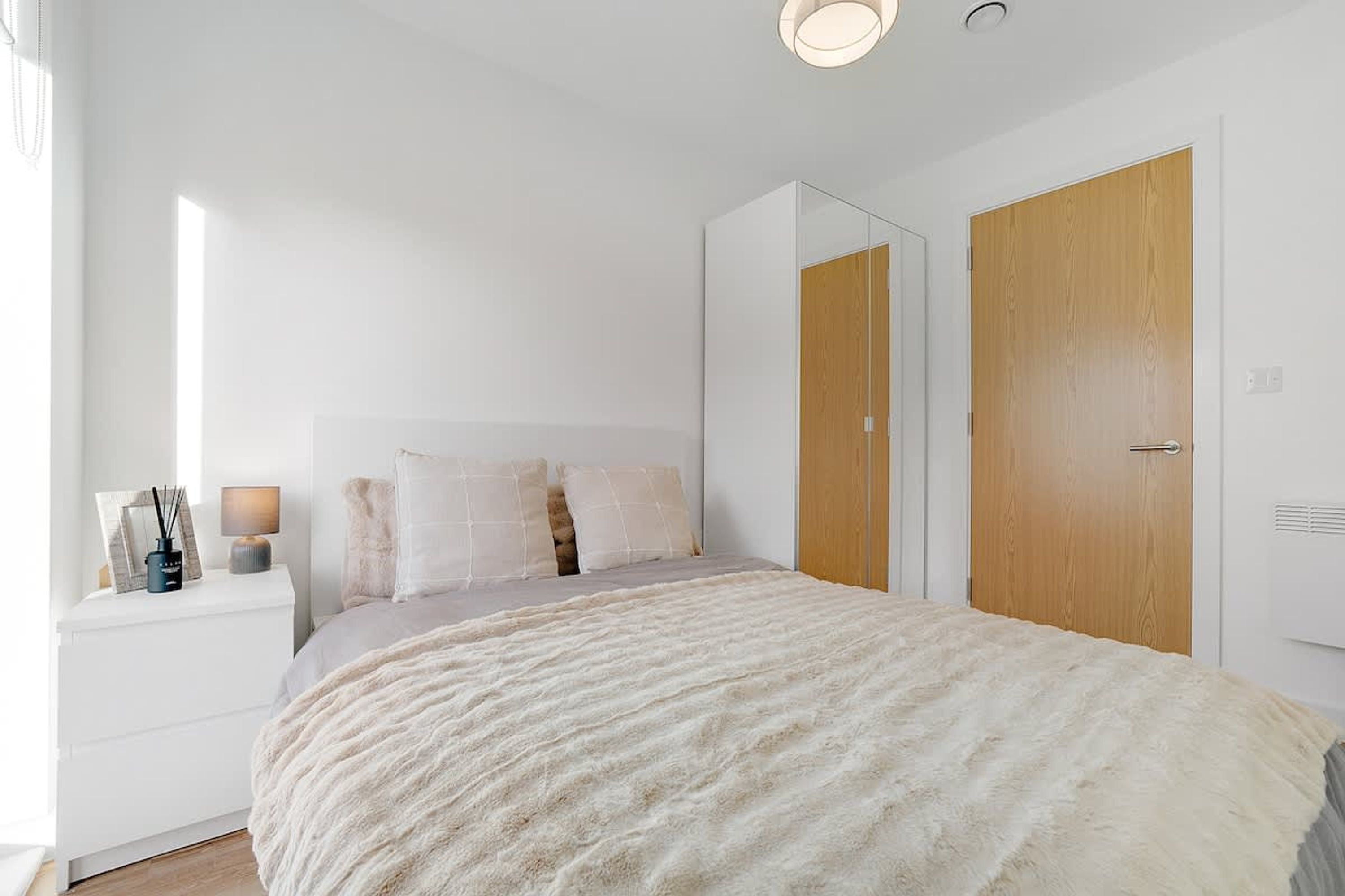 Een slaapkamer met een bed, nachtkastje, spiegel en kledingkast.