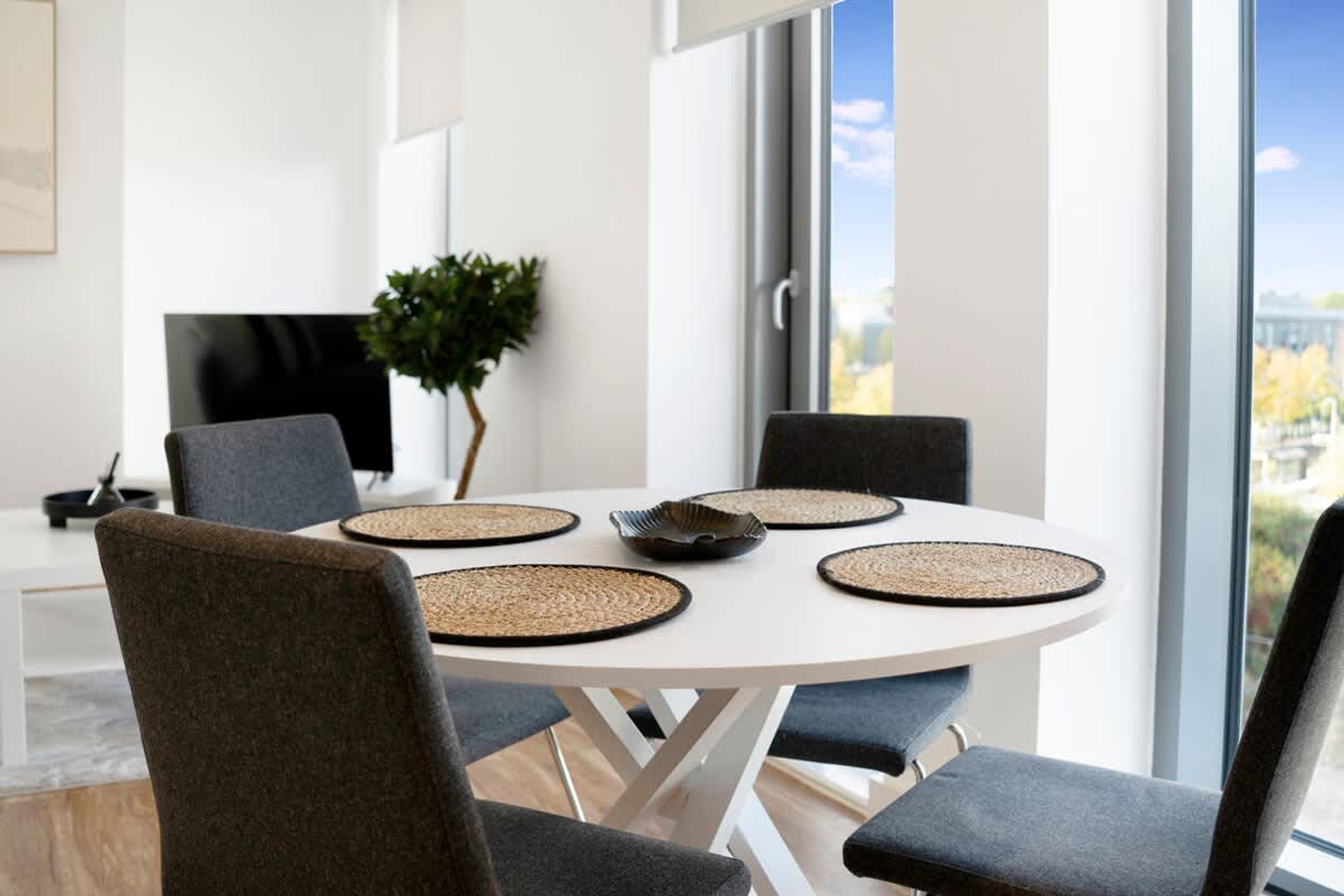 Een moderne eethoek met een ronde tafel, vier stoelen en geweven plaatszetters.