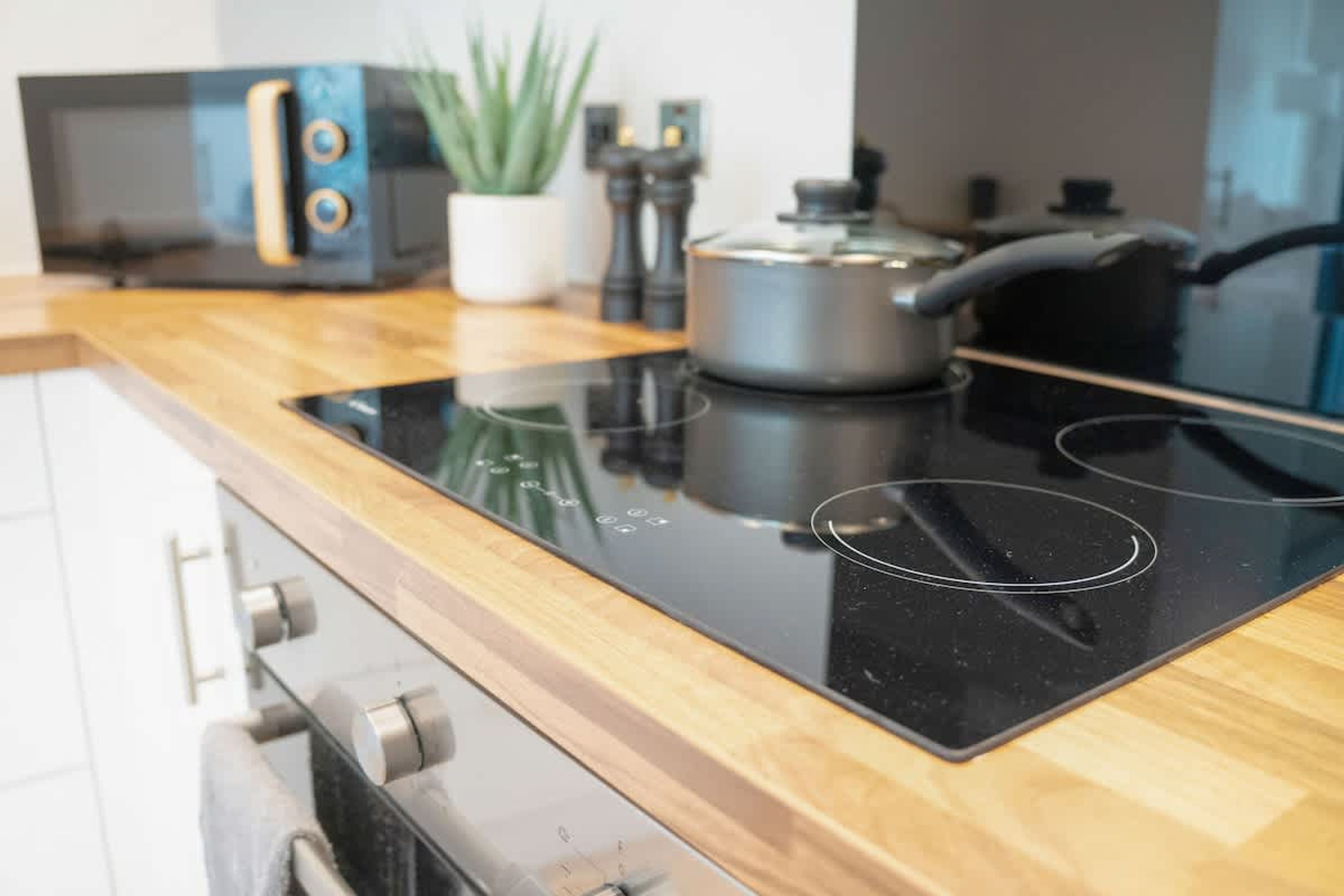 Een keuken met een zwart inductiekookveld, een magnetron, een fornuis en een potplant.