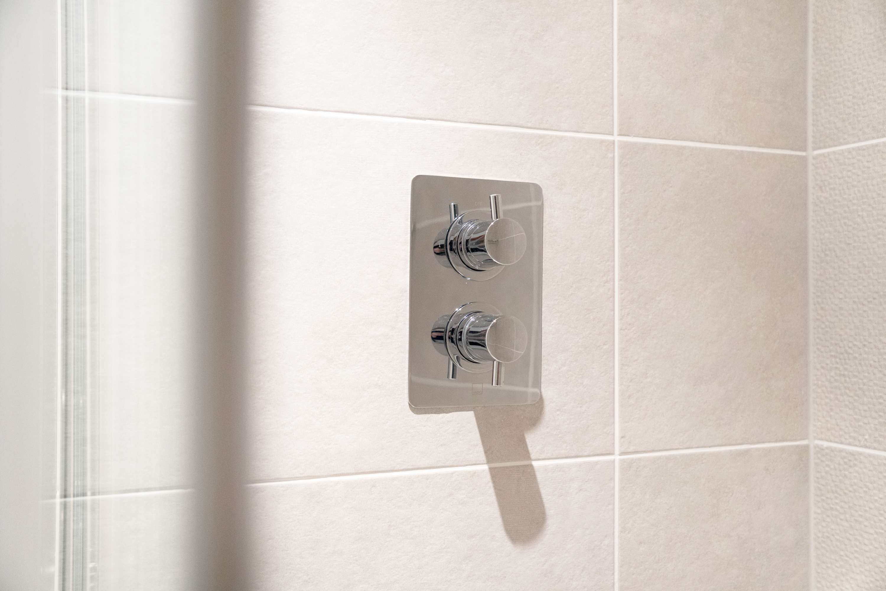 A bathroom with a shower area, featuring a wall-mounted shower control panel with two handles.