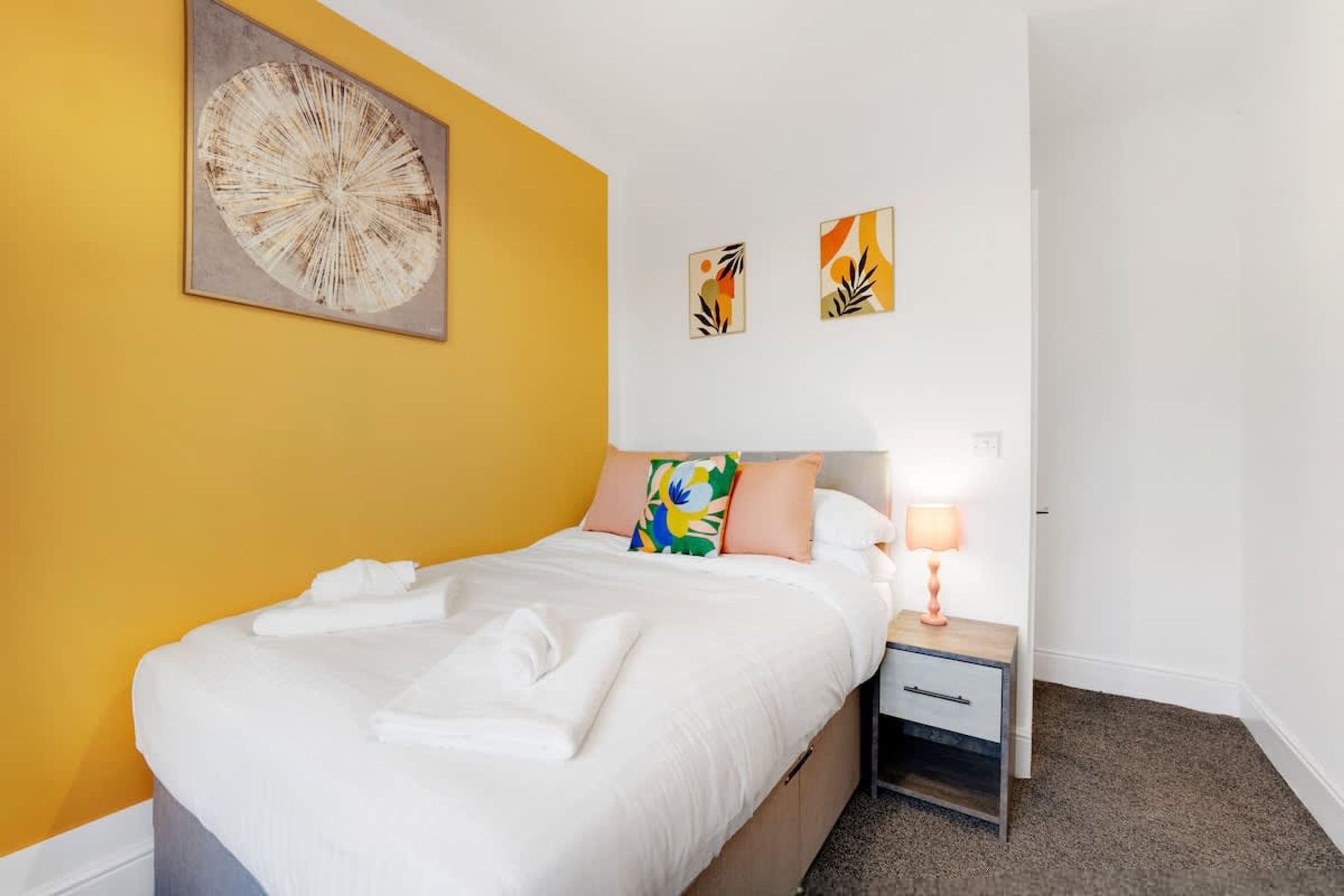 Una habitación de hotel con cama, mesita de noche, lámpara y una obra de arte en la pared.