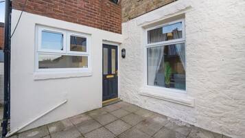 A narrow alleyway with a white wall and a black door, leading to a building with a window.