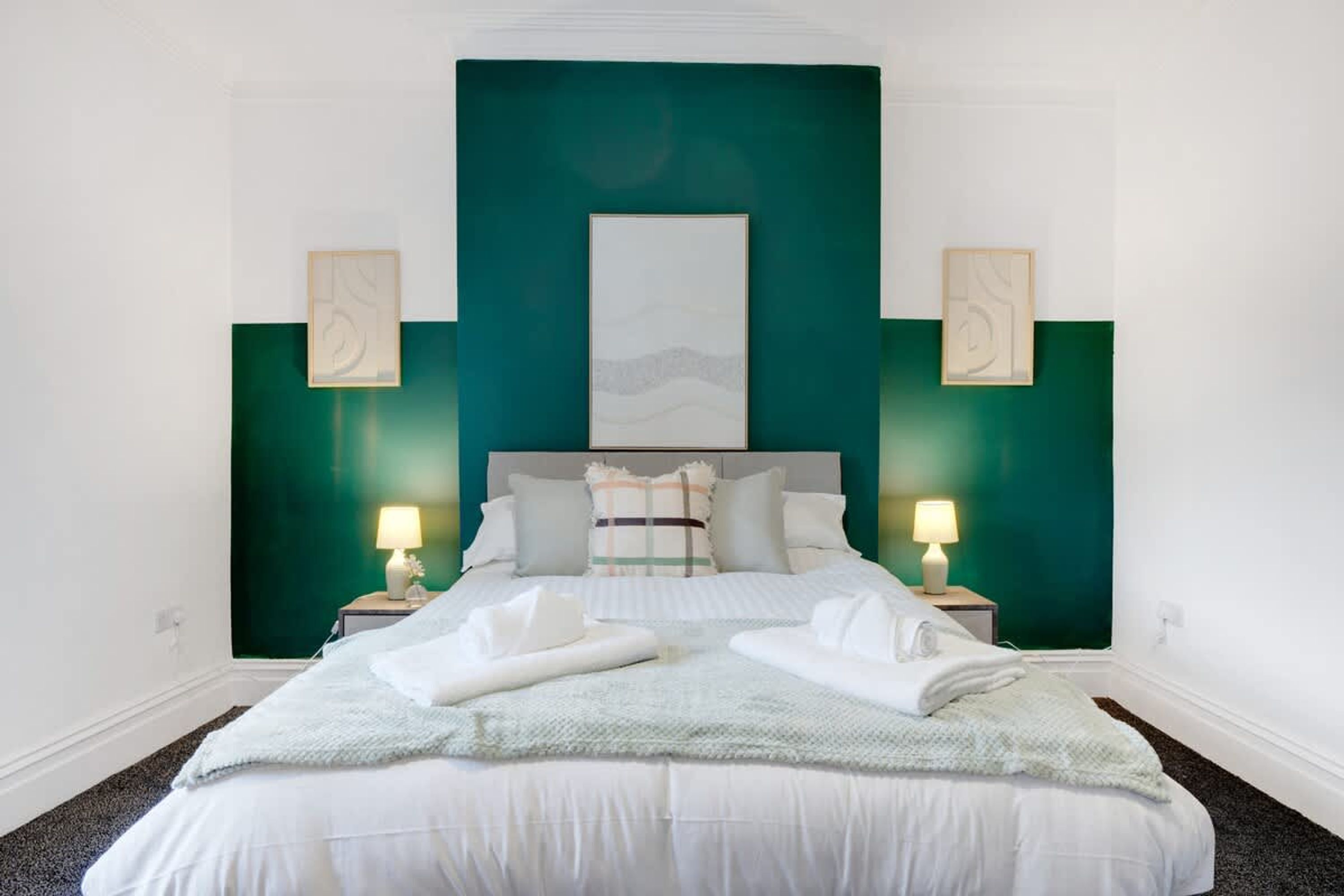 A hotel room with a large bed, two bedside tables with lamps, a headboard, and two wall-mounted artworks.