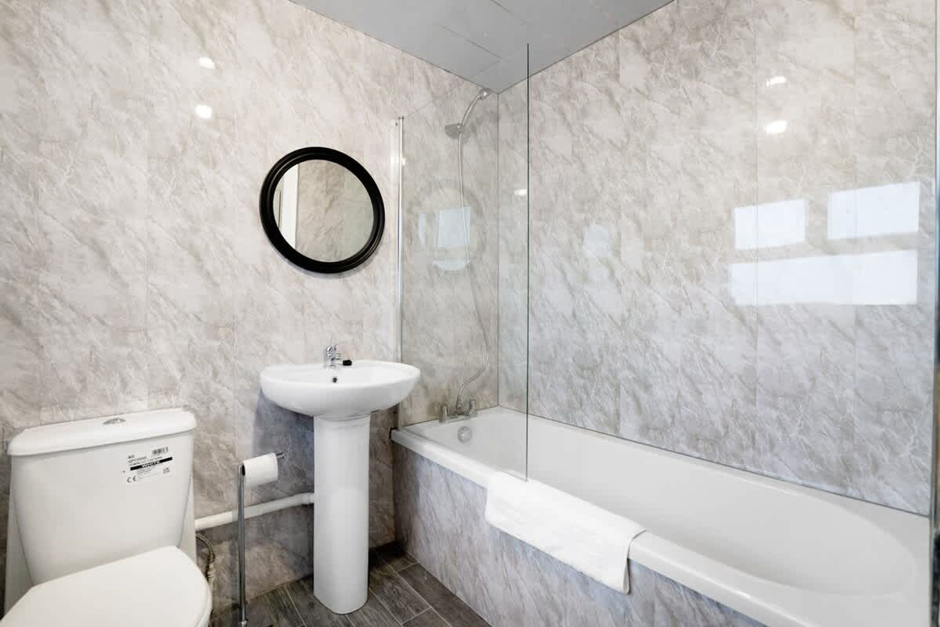 A modern bathroom with a toilet, pedestal sink, and a glass-enclosed shower area.