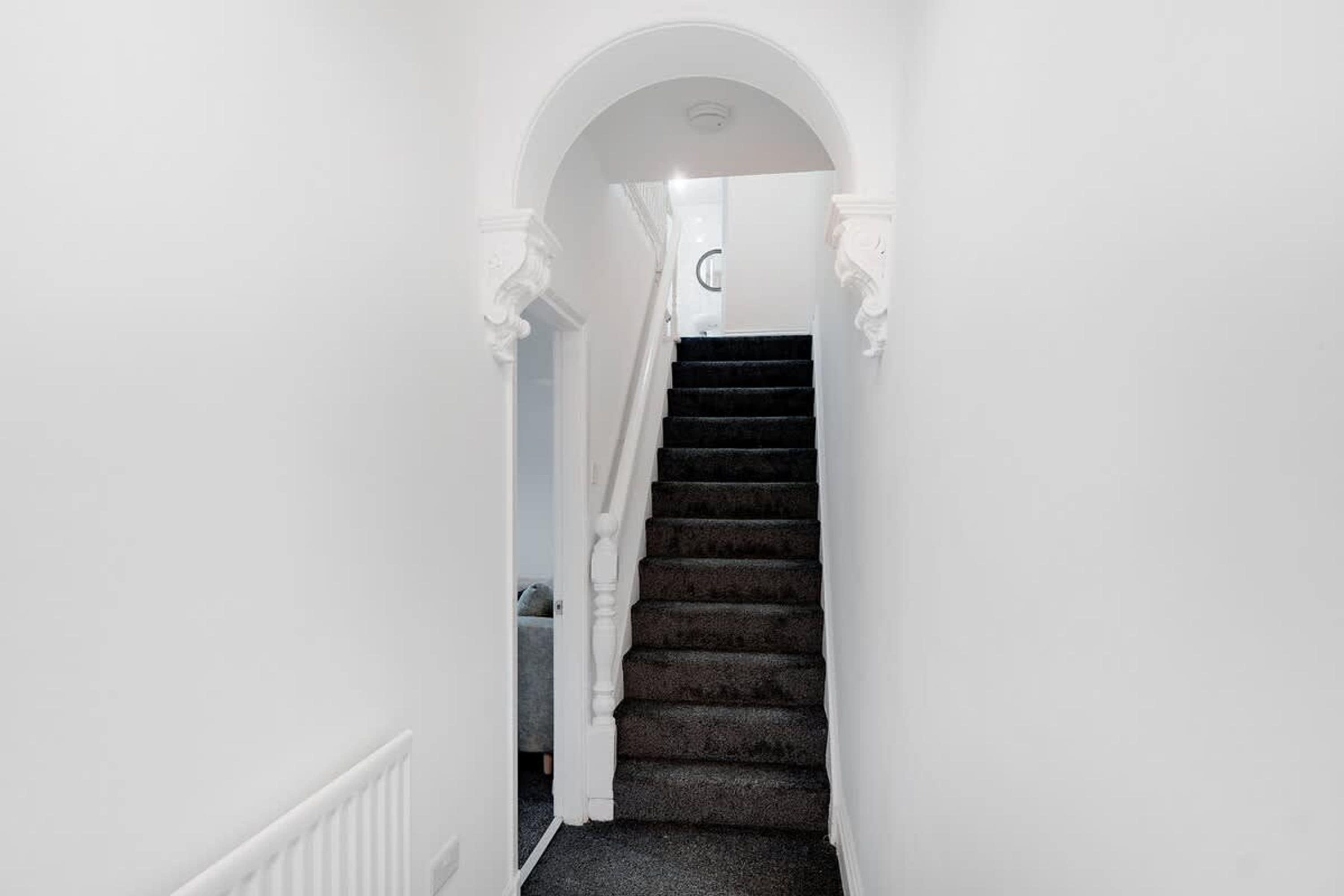 Una escalera con peldaños oscuros cubiertos de alfombra que lleva a un rellano con una puerta blanca.
