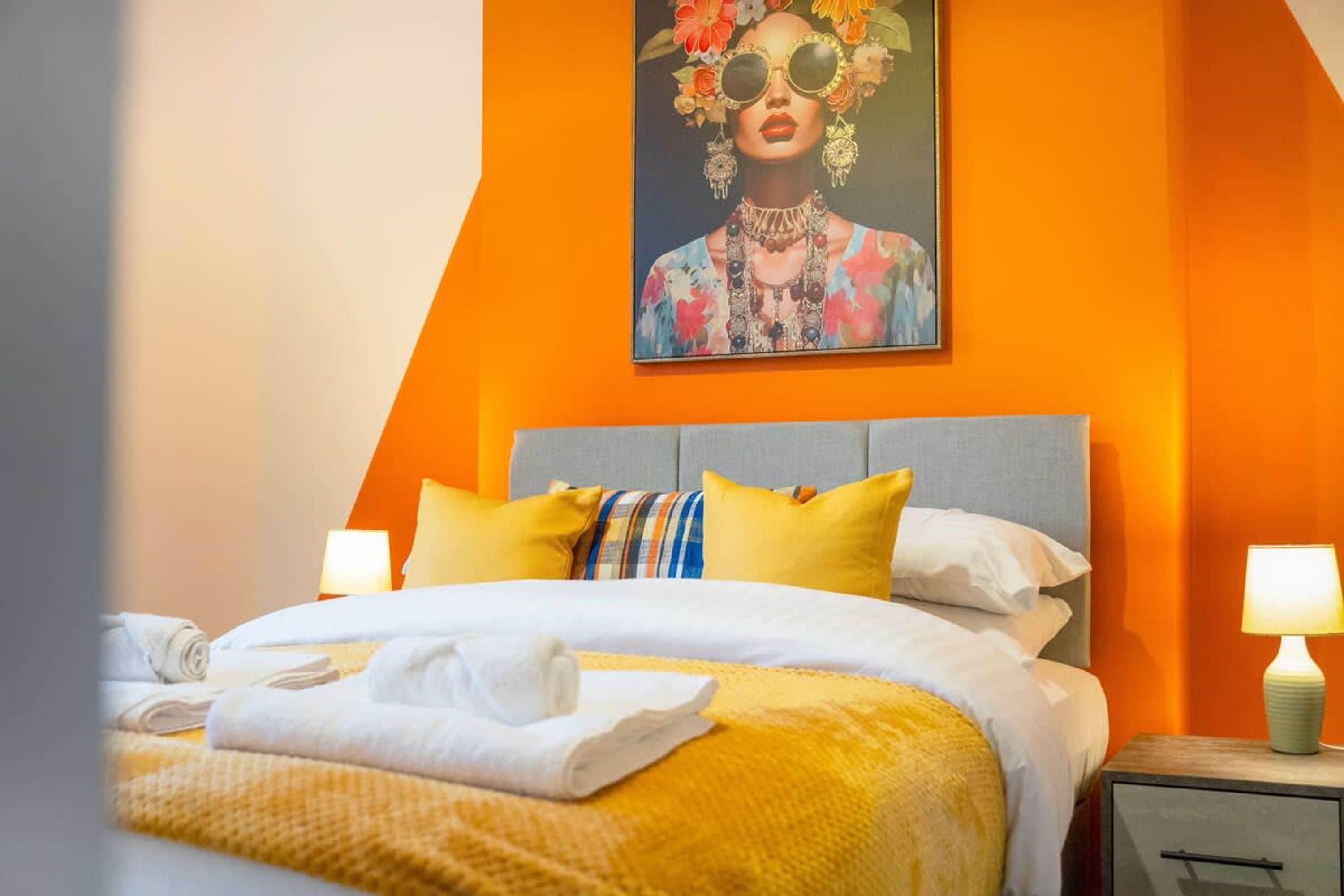 A hotel room with a bed, pillows, a nightstand, and a painting on the wall.