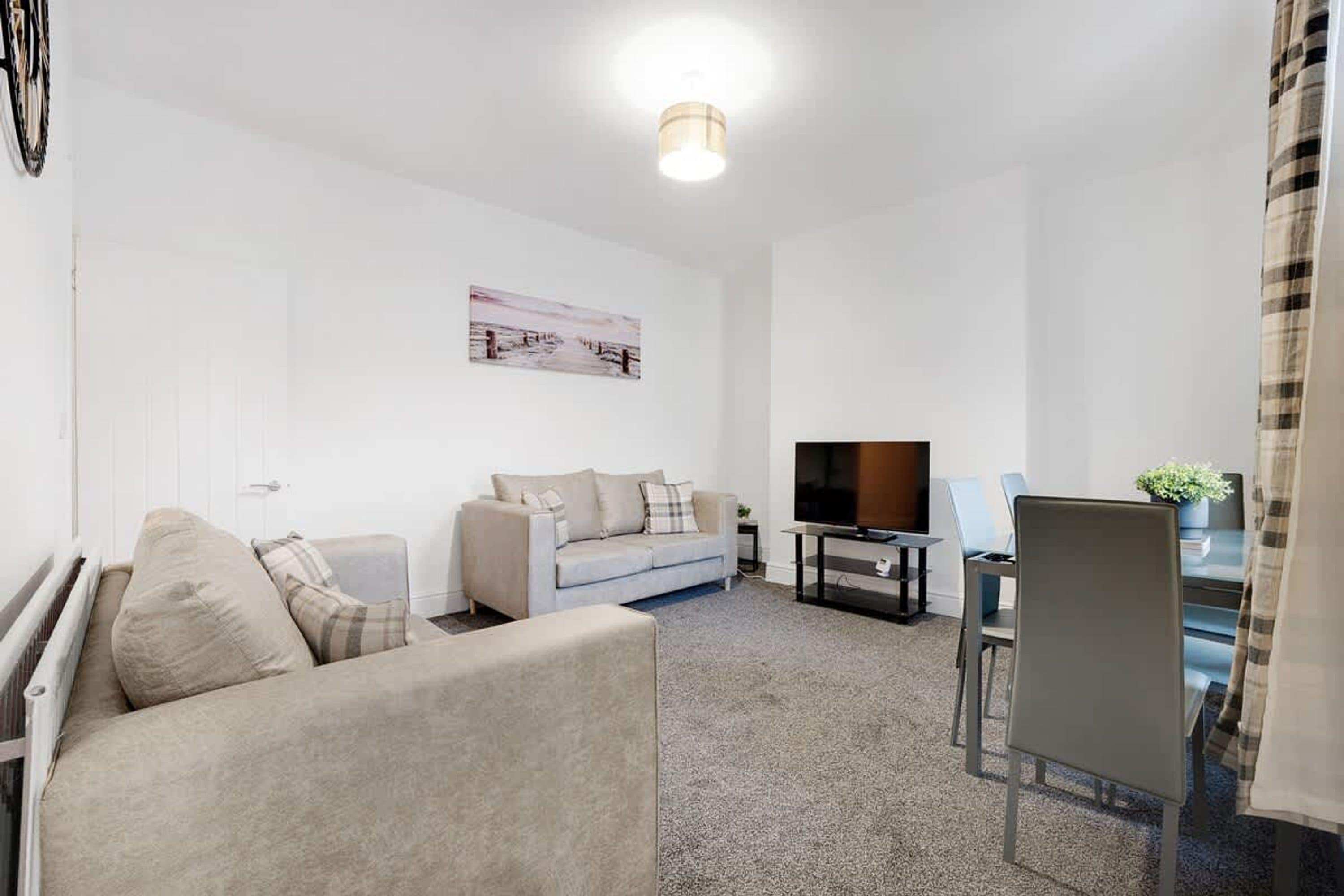 A modern living room with a sofa, a television, and a dining area.
