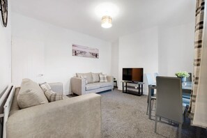 A modern living room with a sofa, a television, and a dining area. - Perfect 4BR for Large Groups Sleeps 7 in Stanley (Stanley)