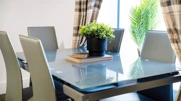 Un salón de conferencias con una mesa de vidrio, cuatro sillas, una planta en maceta y una pila de libros.