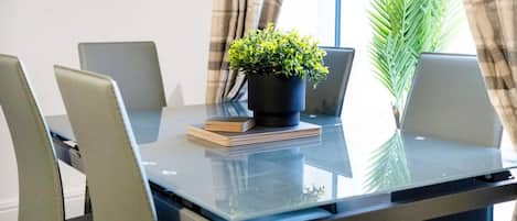 A conference room with a glass table, four chairs, a potted plant, and a stack of books.