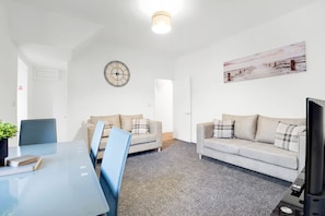 Una habitación con dos sofás, una mesa de comedor, un reloj y un cuadro en la pared.