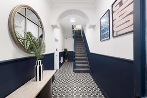 Ein Korridor mit einem Schachbrettmuster auf dem Boden, einem runden Spiegel, einer Treppe und gerahmten Kunstwerken an den Wänden.