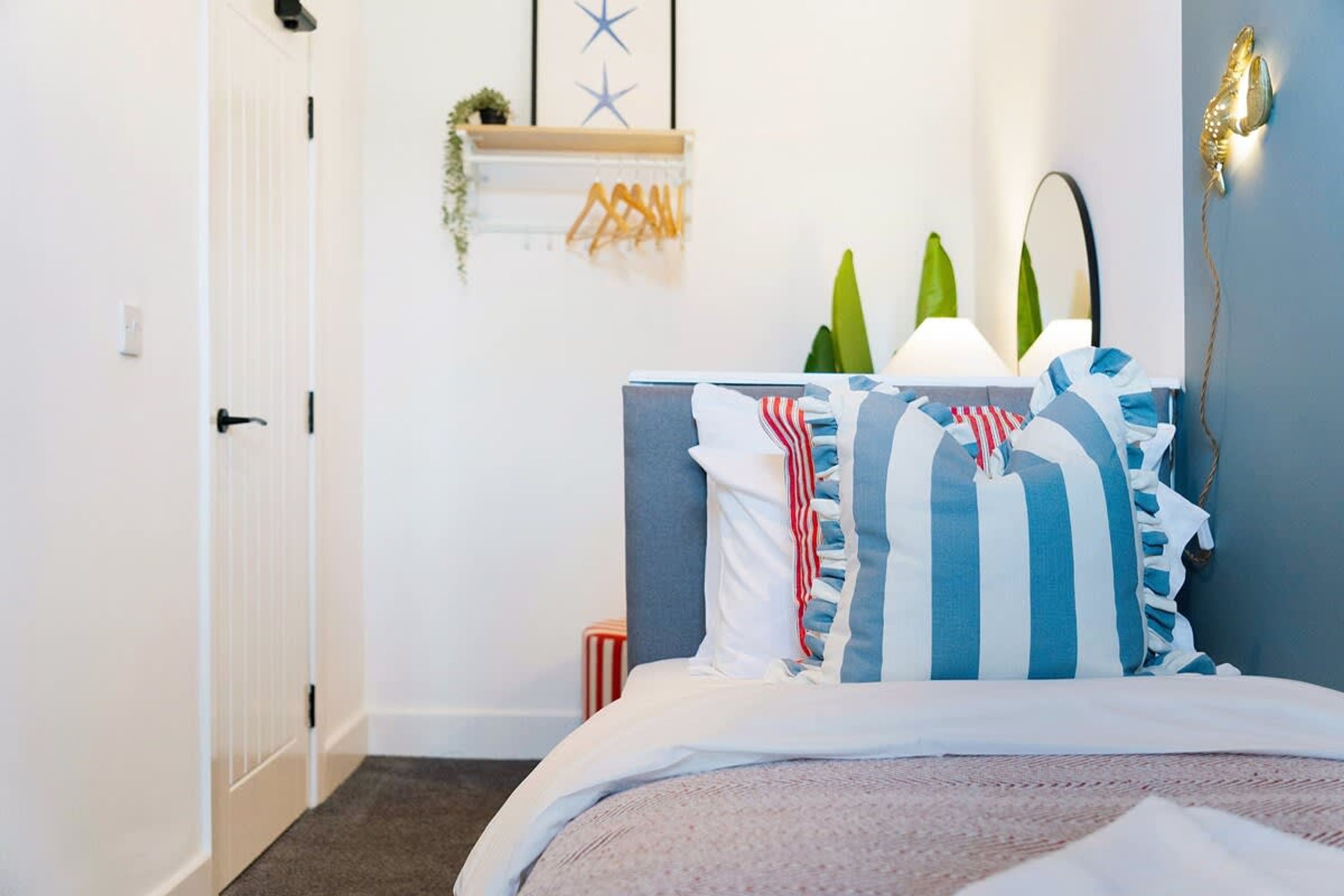 A bedroom with a bed, a bedside table, a lamp, and a wall-mounted shelf with decorative items.