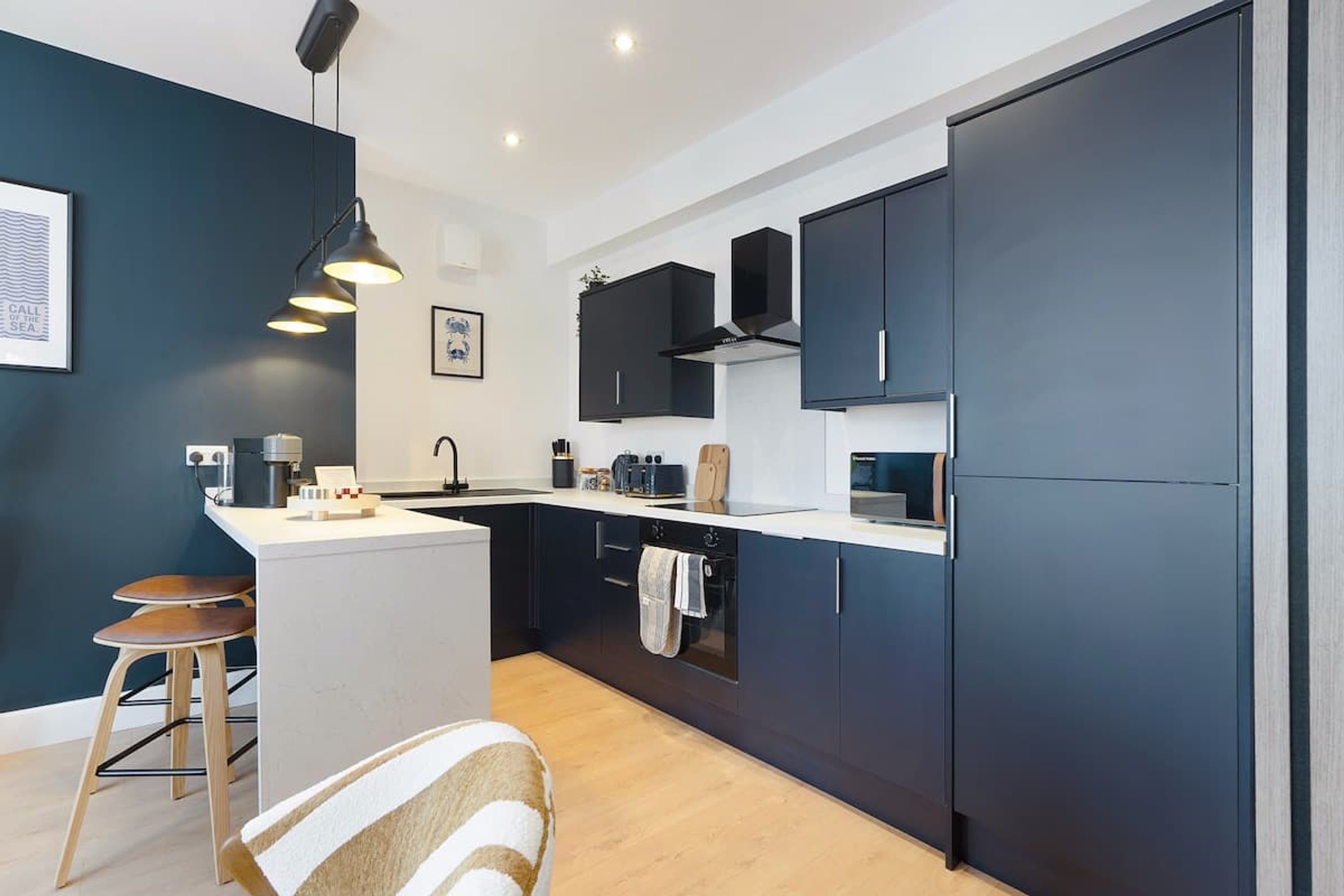 Een moderne keuken met donkere kastjes, een centraal eiland, hanglampen en een houten vloer.