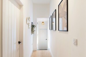 A hallway with white walls, a wooden door, and framed artwork on the walls. - High-spec Hartlepool 3BR Apartment Sleeps 5 by Stay With Us (Hartlepool)