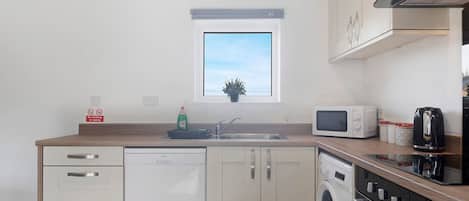 A compact kitchen with a dishwasher, microwave, stove, and a window above the sink.