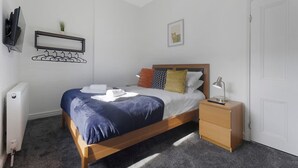 Ein ordentlich eingerichtetes Schlafzimmer mit einem Bett, einem Nachttisch und einem an der Wand befestigten Kleiderhaken.