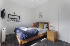 Ein ordentlich eingerichtetes Schlafzimmer mit einem Bett, einem Nachttisch und einem an der Wand befestigten Kleiderhaken.