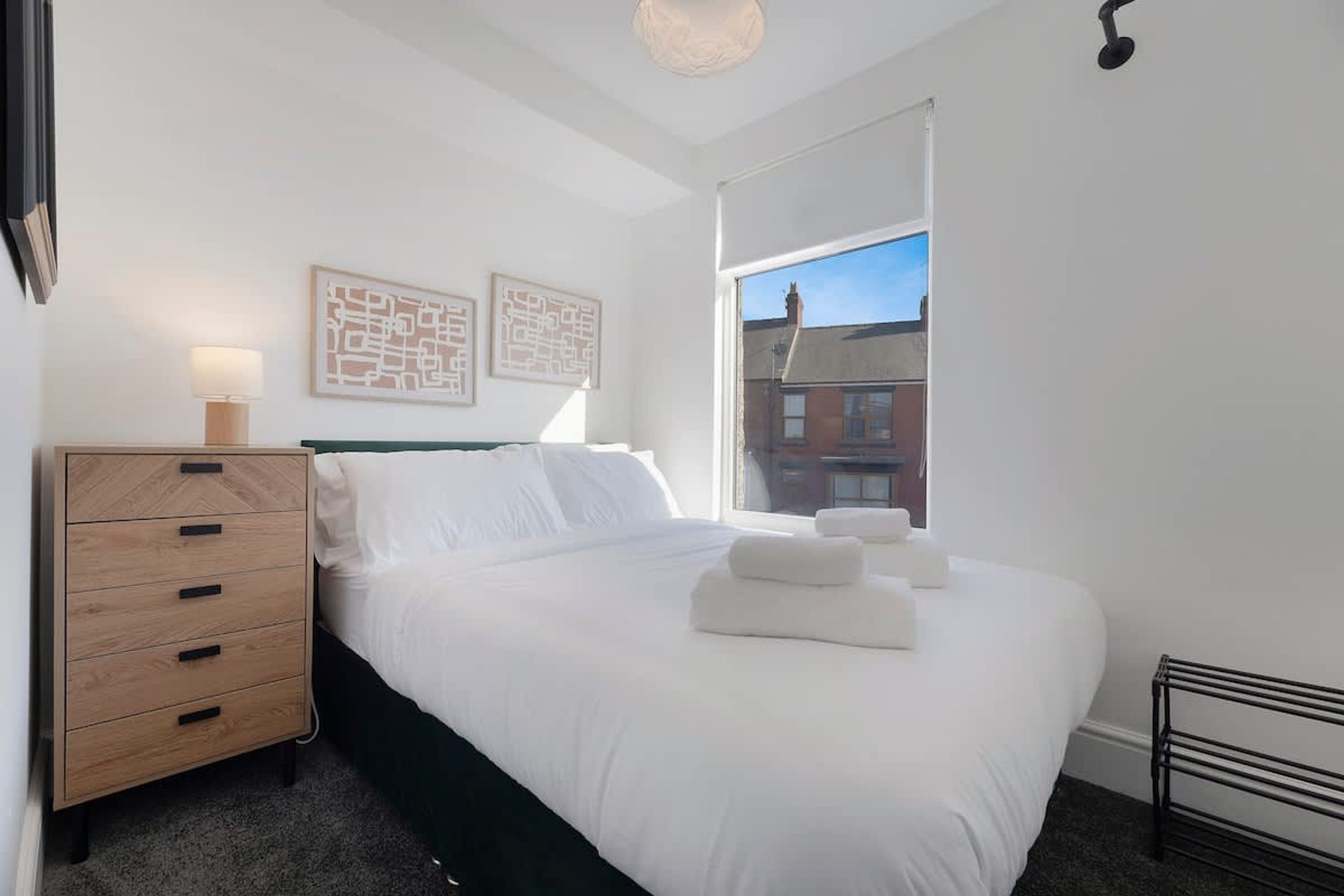 A bedroom with a bed, a dresser, a window, and artwork on the wall.