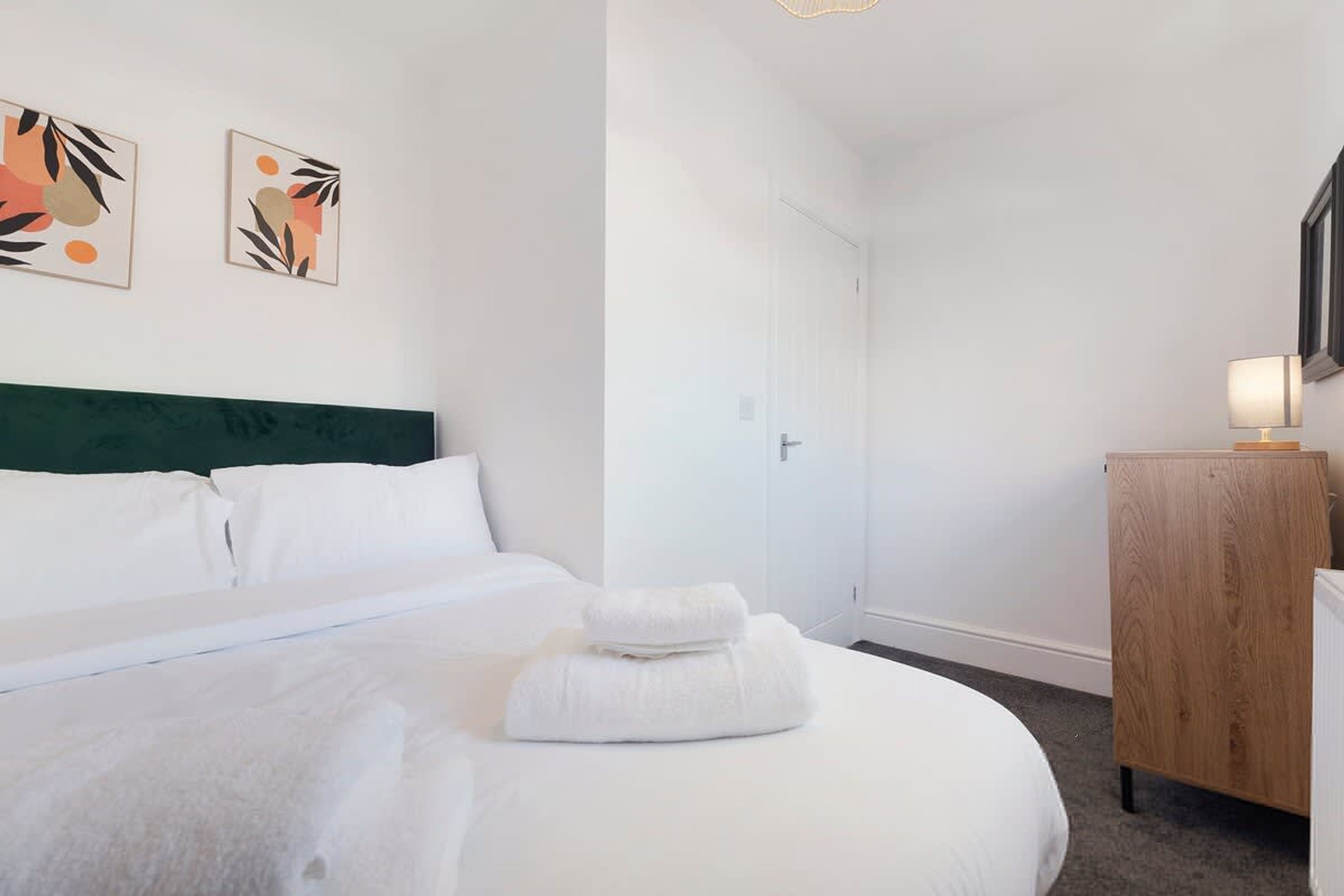 Une chambre d’hôtel avec un lit, une commode en bois et deux œuvres d’art accrochées au mur.