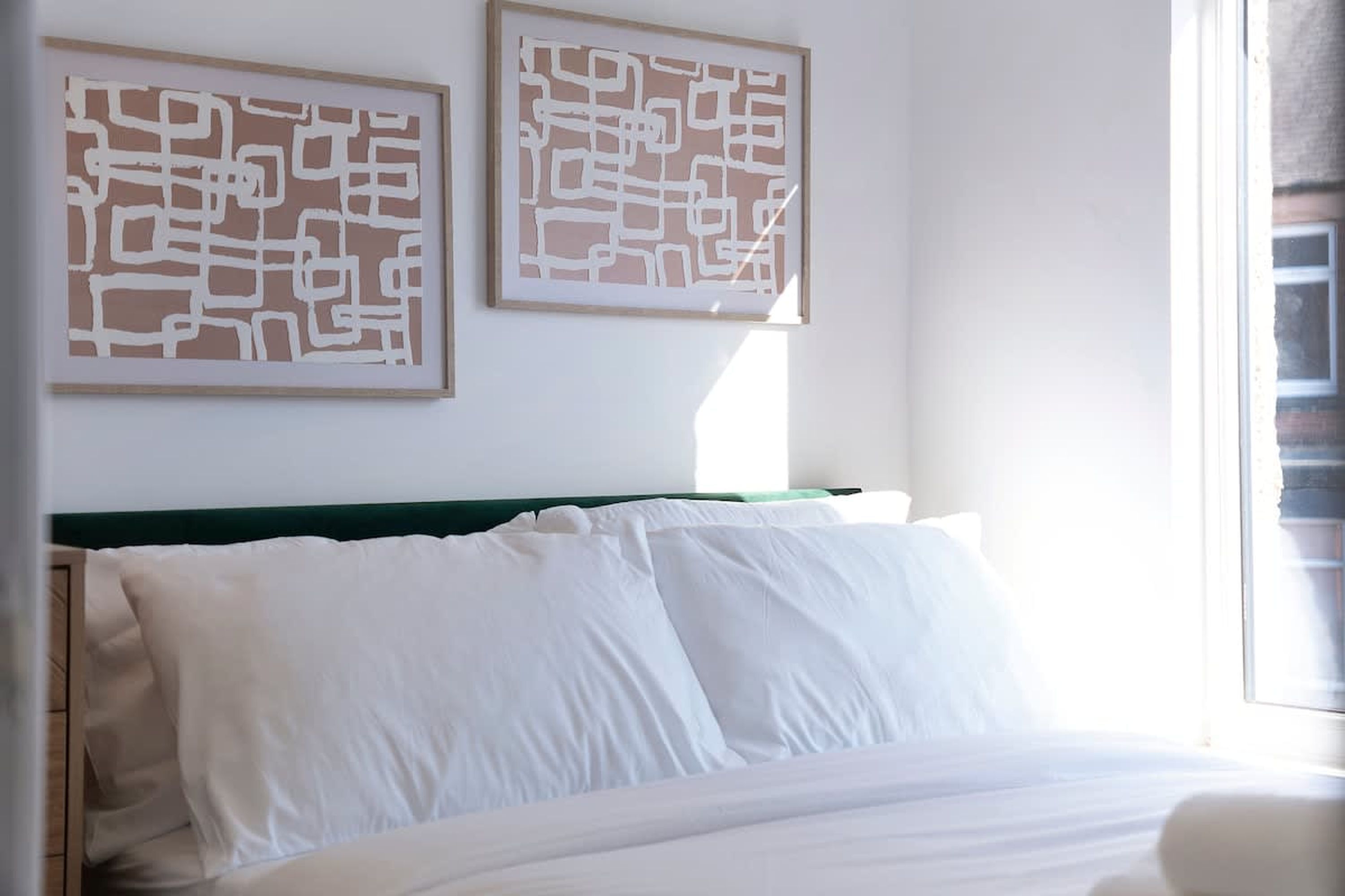 Une chambre d’hôtel avec un lit, des oreillers blancs et deux œuvres d’art abstraites accrochées au mur.