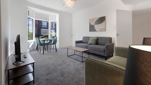 A modern living room with a grey sofa, a coffee table, a TV, and a dining area with chairs and a table. - Spacious Retreat at Durham Road (Spennymoor)