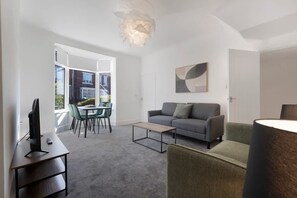 Ein modernes Wohnzimmer mit einem grauen Sofa, einem Couchtisch, einem Fernseher und einem Essbereich mit Stühlen und Tisch.