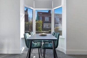 Ein Eckzimmer mit Erkerfenster, einem Esstisch mit Stühlen und Blick auf benachbarte Häuser.
