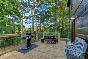 A wooden deck with a grill, picnic table, and bench, surrounded by trees. - Bears on Beach Front * 3 beds * 2 bath * sleeps 9 (Sevierville)