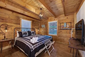 A wooden cabin bedroom with a bed, two windows, a chandelier, a desk, and a television. - Bears on Beach Front * 3 beds * 2 bath * sleeps 9 (Sevierville)