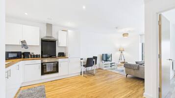 Cocina moderna con armarios blancos, microondas y estufa. Cuenta con un comedor con mesa y sillas, y un sofá en la sala.