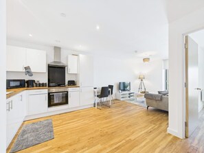 Cocina moderna con armarios blancos, microondas y estufa. Cuenta con un comedor con mesa y sillas, y un sofá en la sala.