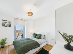 Un dormitorio moderno con cama, vistas a la ciudad, una lámpara de techo y una planta.