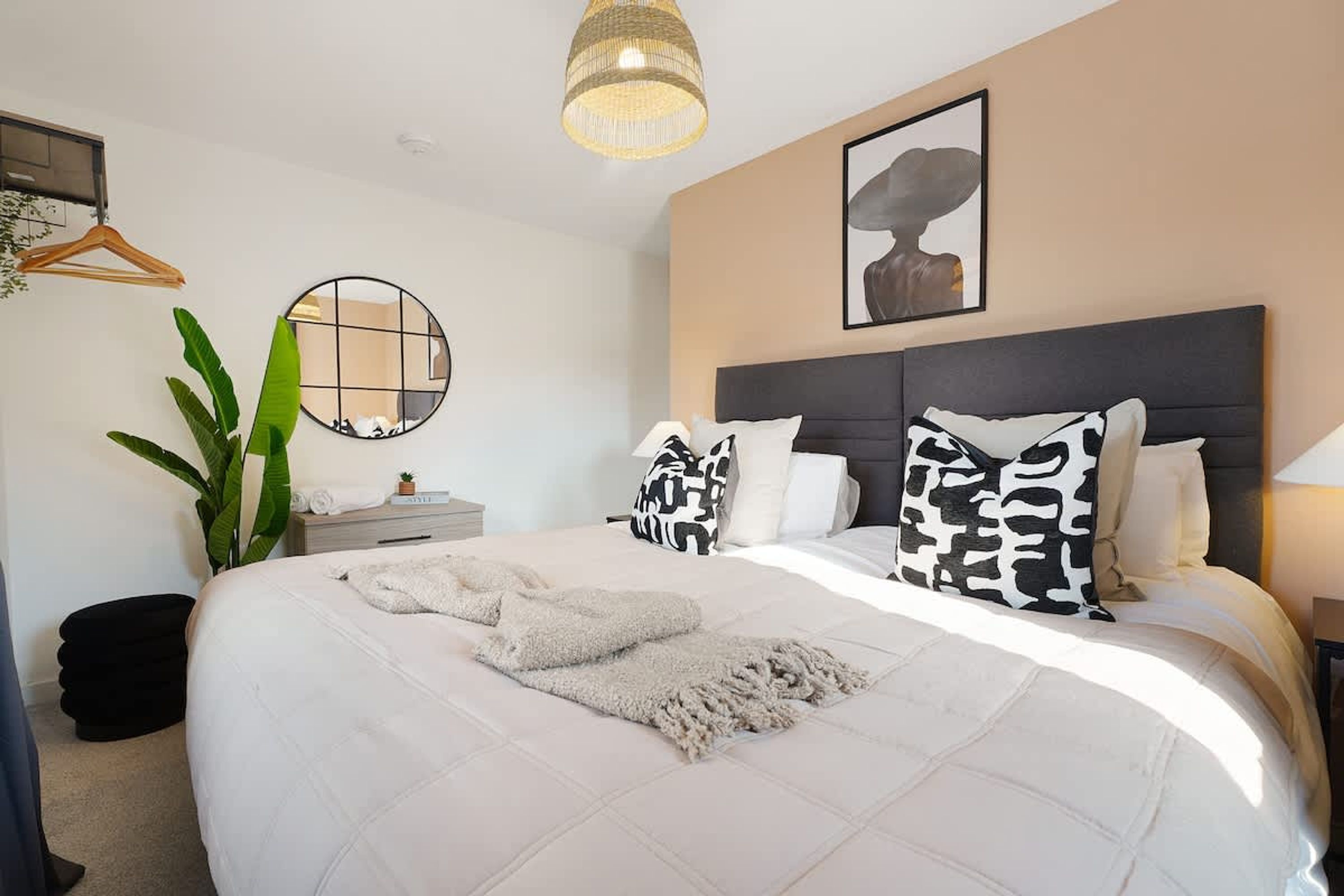 A bedroom with a large bed, a round mirror, a hanging light fixture, a framed artwork, and a potted plant.