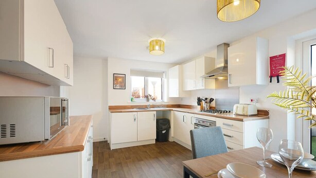 Una cocina moderna con armarios blancos, encimera de madera y una zona de comedor con una mesa lista para dos.