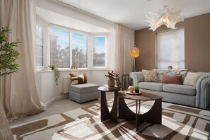 Ein modernes Wohnzimmer mit Sofa, Couchtisch und Lampe. Es gibt Fenster mit Jalousien, eine Heizung und eine Pflanze.