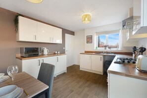Een moderne keuken met witte kasten, een magnetron, een waterkoker en een eethoek met een tafel en stoelen.