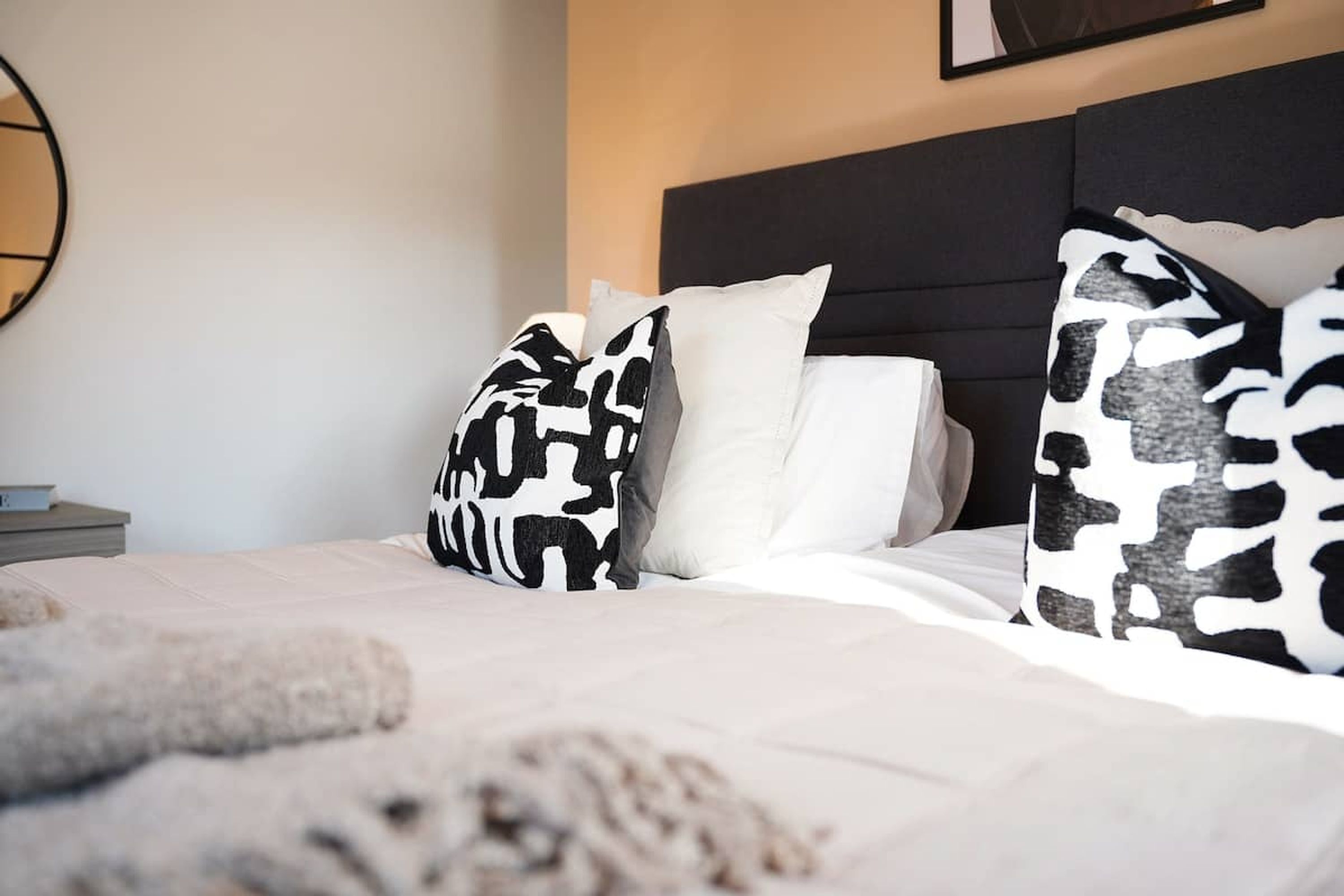 A bed with patterned pillows, a white pillow, and a headboard.